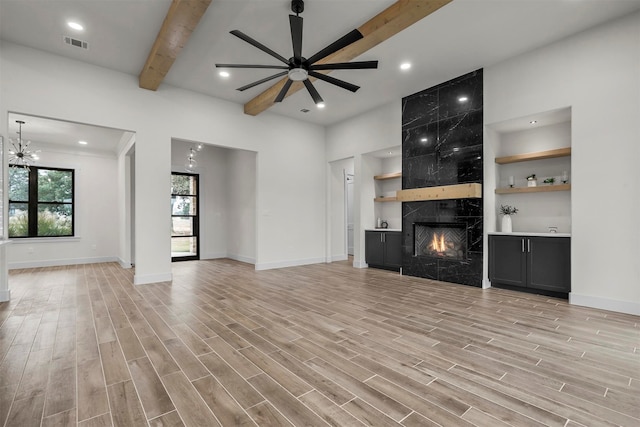 unfurnished living room with a premium fireplace, light hardwood / wood-style flooring, beamed ceiling, and ceiling fan with notable chandelier