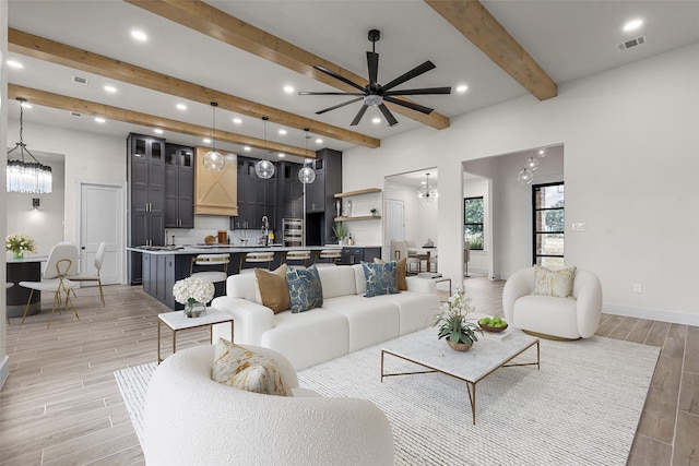 living room with beamed ceiling, light hardwood / wood-style flooring, and ceiling fan with notable chandelier