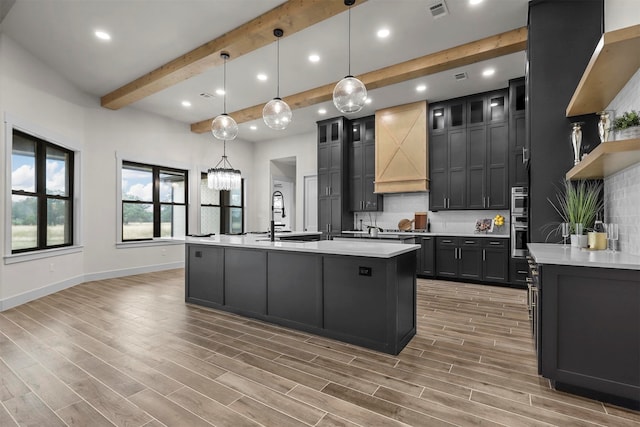 kitchen featuring custom range hood, pendant lighting, decorative backsplash, sink, and an island with sink