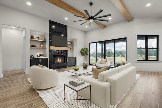 living room with ceiling fan, a premium fireplace, light hardwood / wood-style flooring, built in features, and lofted ceiling with beams