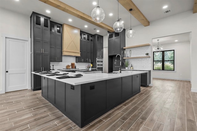 kitchen with beamed ceiling, sink, hardwood / wood-style floors, a spacious island, and pendant lighting