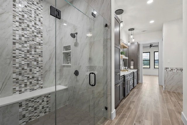 bathroom featuring a shower with door, ceiling fan, wood-type flooring, vanity, and tile walls