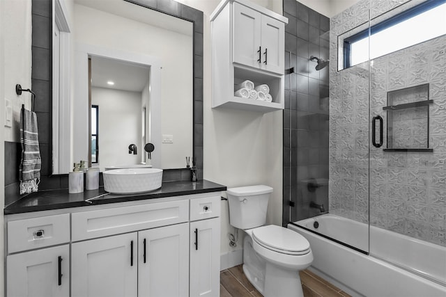 full bathroom with hardwood / wood-style floors, bath / shower combo with glass door, vanity, and toilet