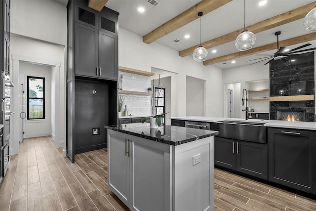 kitchen featuring wood-type flooring, a kitchen island, beam ceiling, a fireplace, and dark stone countertops