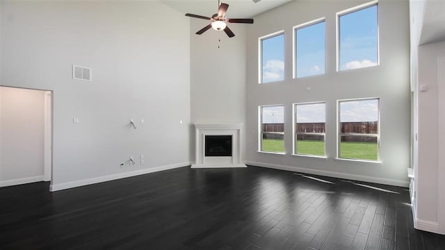 unfurnished living room with dark hardwood / wood-style flooring, a healthy amount of sunlight, a high ceiling, and ceiling fan