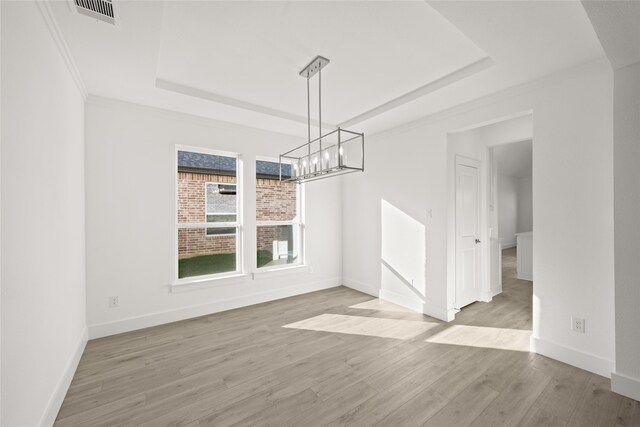 unfurnished dining area with a tray ceiling, crown molding, and light wood-type flooring