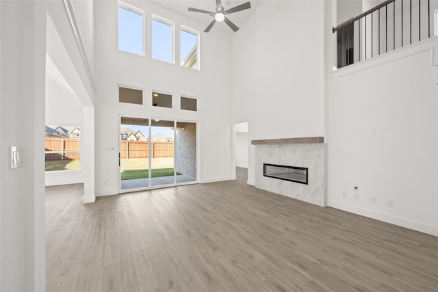 unfurnished living room with a fireplace, ceiling fan, hardwood / wood-style floors, and a towering ceiling