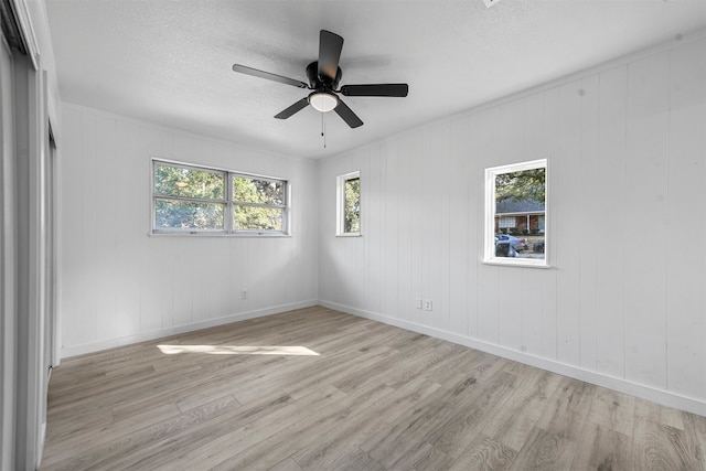 unfurnished room with wooden walls, ceiling fan, and light hardwood / wood-style flooring