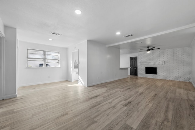 unfurnished living room featuring a fireplace, light hardwood / wood-style floors, ceiling fan, and brick wall