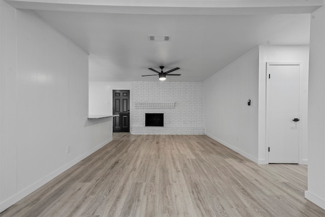 unfurnished living room featuring a fireplace, light hardwood / wood-style floors, ceiling fan, and brick wall