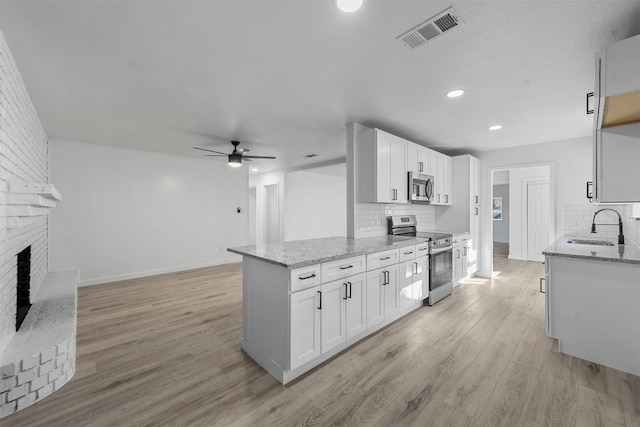 kitchen with stainless steel appliances, white cabinetry, sink, and light stone counters