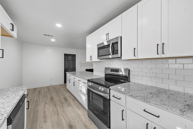 kitchen with stainless steel appliances, decorative backsplash, light stone countertops, white cabinetry, and light wood-type flooring