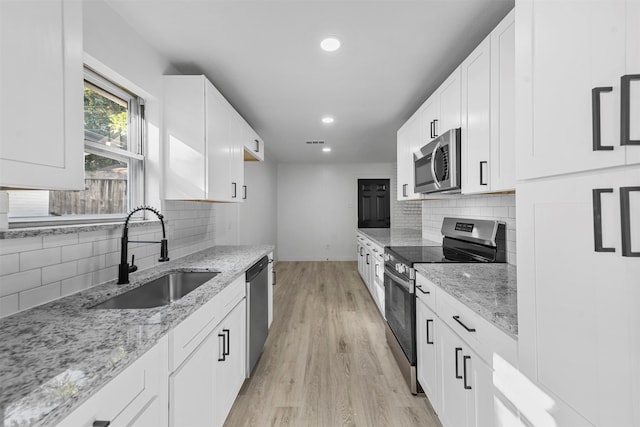 kitchen featuring light stone counters, stainless steel appliances, white cabinetry, sink, and light hardwood / wood-style flooring