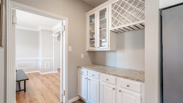 kitchen featuring white cabinets, light wood-type flooring, light stone counters, and crown molding