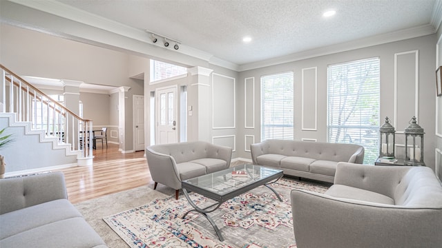 living room featuring light hardwood / wood-style floors, a textured ceiling, decorative columns, ornamental molding, and rail lighting