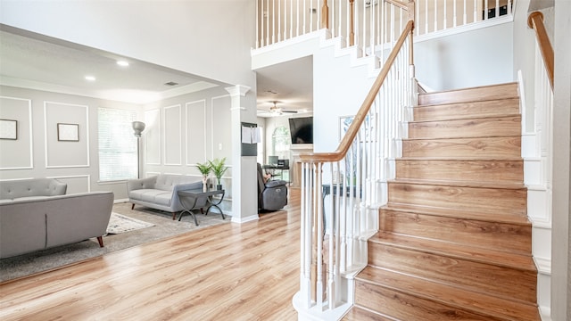 stairs with ceiling fan, hardwood / wood-style floors, a towering ceiling, crown molding, and ornate columns