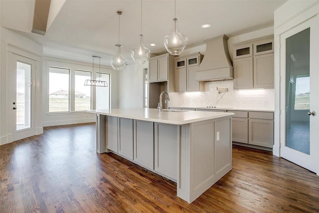 kitchen with an island with sink, glass insert cabinets, light countertops, premium range hood, and a sink