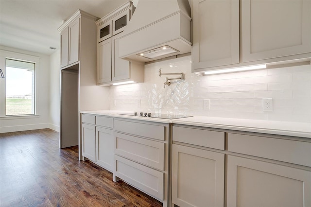 kitchen with glass insert cabinets, light countertops, premium range hood, and black electric cooktop