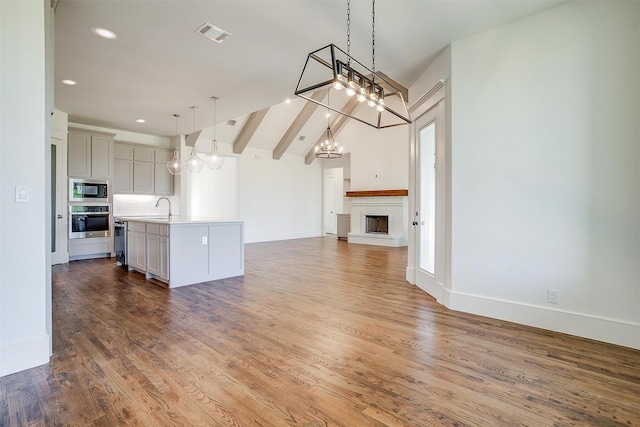 kitchen featuring oven, open floor plan, light countertops, built in microwave, and a center island with sink