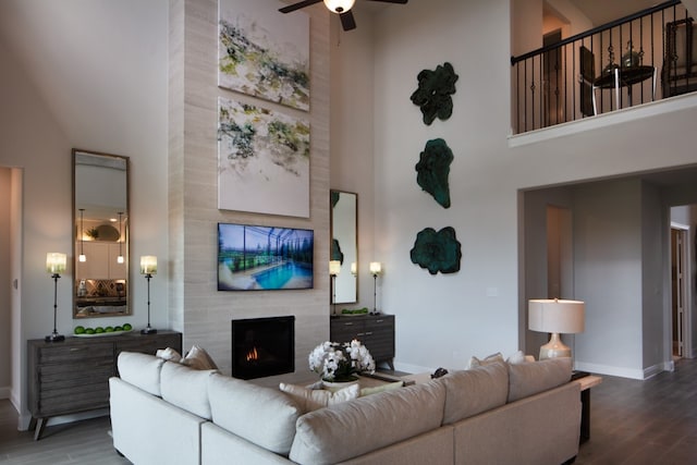 living room with a high ceiling, wood-type flooring, ceiling fan, and a fireplace