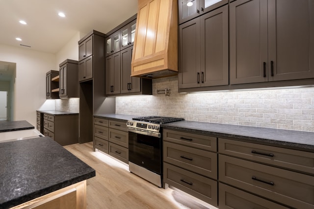 kitchen featuring light wood-type flooring, custom exhaust hood, gas range, and decorative backsplash