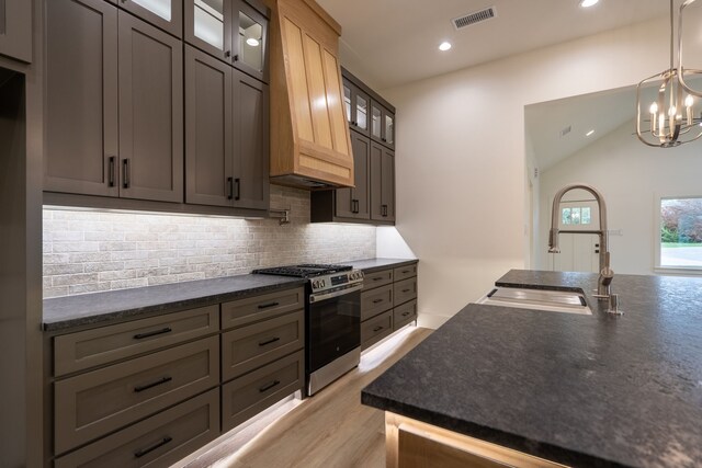 kitchen with vaulted ceiling, stainless steel range with gas stovetop, sink, tasteful backsplash, and premium range hood