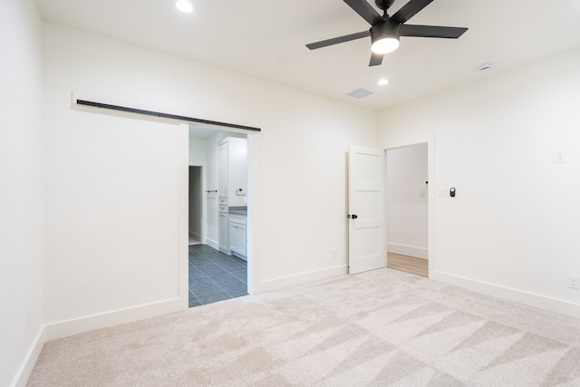 unfurnished bedroom featuring a barn door, ceiling fan, connected bathroom, and carpet