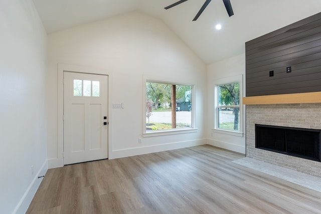 unfurnished living room featuring high vaulted ceiling, light wood-type flooring, ceiling fan, and a brick fireplace