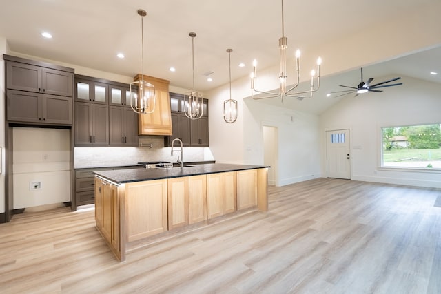 kitchen featuring decorative backsplash, sink, vaulted ceiling, light hardwood / wood-style floors, and a kitchen island with sink