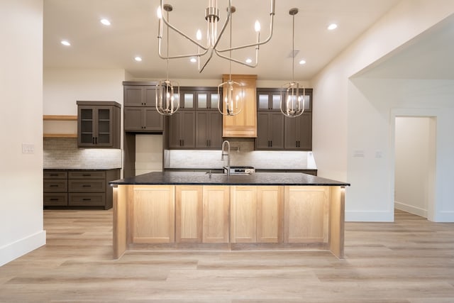 kitchen featuring tasteful backsplash, a center island with sink, sink, light hardwood / wood-style floors, and dark stone countertops