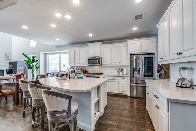 kitchen with white cabinetry, appliances with stainless steel finishes, tasteful backsplash, a kitchen island with sink, and dark wood-type flooring