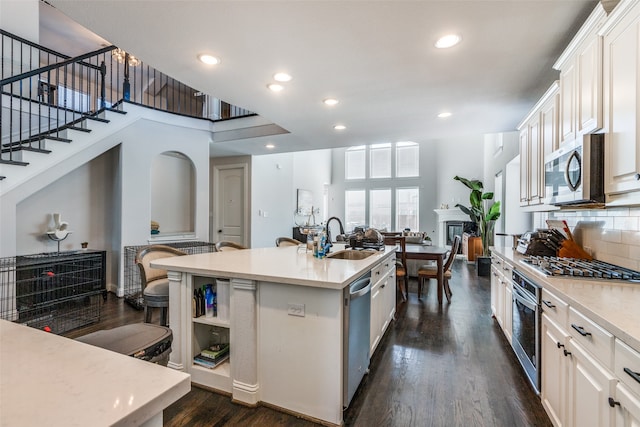 kitchen with stainless steel appliances, a center island with sink, sink, white cabinetry, and dark hardwood / wood-style floors