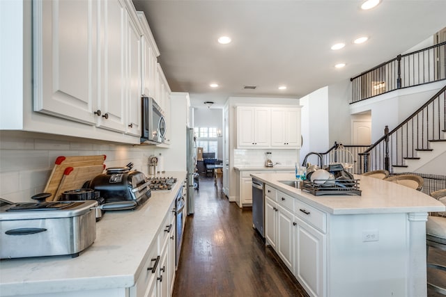 kitchen with white cabinetry, appliances with stainless steel finishes, dark hardwood / wood-style floors, a kitchen island with sink, and decorative backsplash