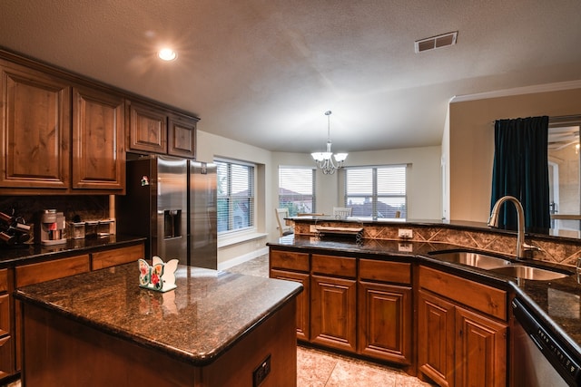 kitchen with sink, appliances with stainless steel finishes, a textured ceiling, a notable chandelier, and a center island