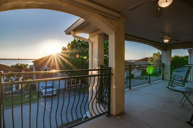 balcony at dusk with a water view and ceiling fan