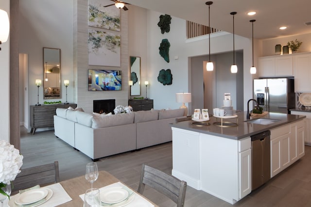 kitchen featuring white cabinets, a towering ceiling, stainless steel appliances, and a center island with sink