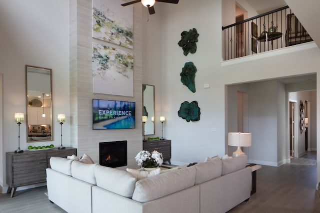 living room with a towering ceiling, a fireplace, hardwood / wood-style flooring, and ceiling fan