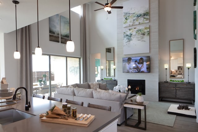 living room with a fireplace, a towering ceiling, sink, hardwood / wood-style flooring, and ceiling fan