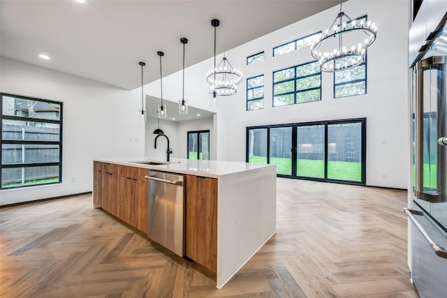 kitchen featuring appliances with stainless steel finishes, sink, light parquet flooring, hanging light fixtures, and an island with sink