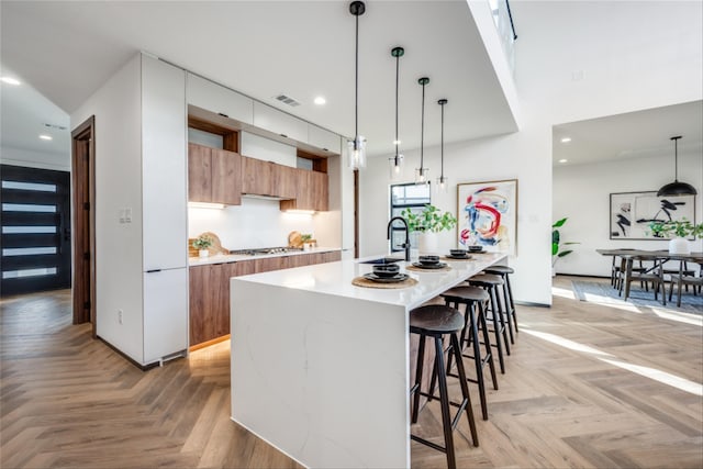 kitchen featuring light parquet floors, an island with sink, hanging light fixtures, and a kitchen breakfast bar