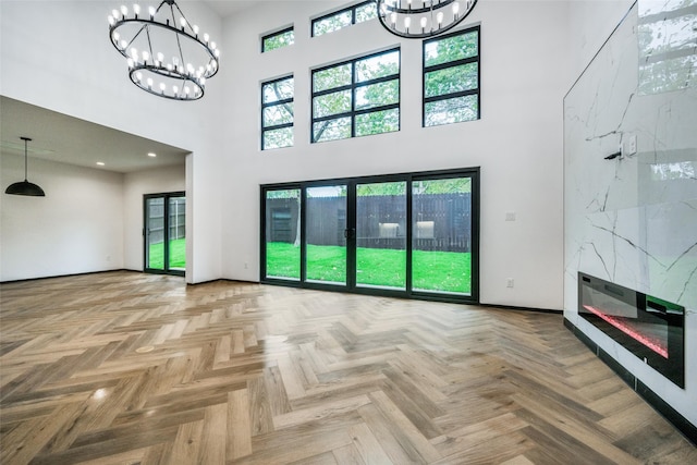 unfurnished living room with a fireplace, light parquet floors, a towering ceiling, and a chandelier