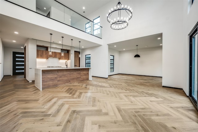 unfurnished living room featuring a towering ceiling, light parquet floors, a notable chandelier, and sink