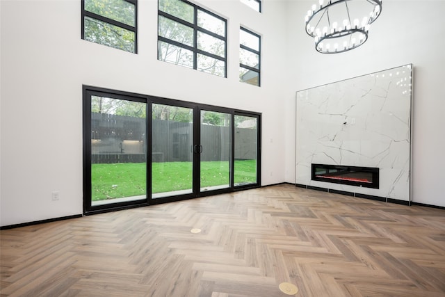 unfurnished living room with a fireplace, a high ceiling, light parquet flooring, and a healthy amount of sunlight