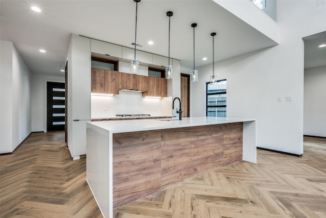 kitchen featuring gas cooktop, tasteful backsplash, an island with sink, decorative light fixtures, and light parquet flooring