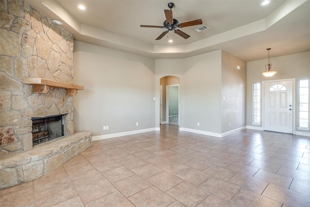 unfurnished living room featuring ceiling fan, a fireplace, a raised ceiling, and light tile patterned floors