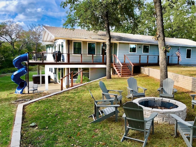 back of property with a deck, a lawn, and an outdoor fire pit