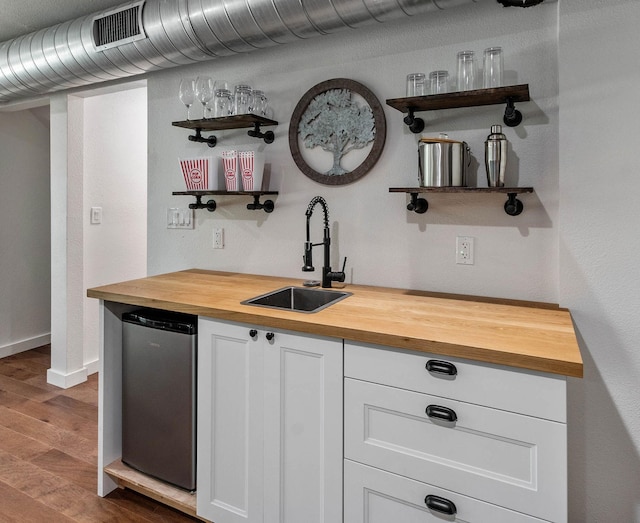 bar featuring butcher block counters, white cabinets, hardwood / wood-style flooring, sink, and stainless steel fridge