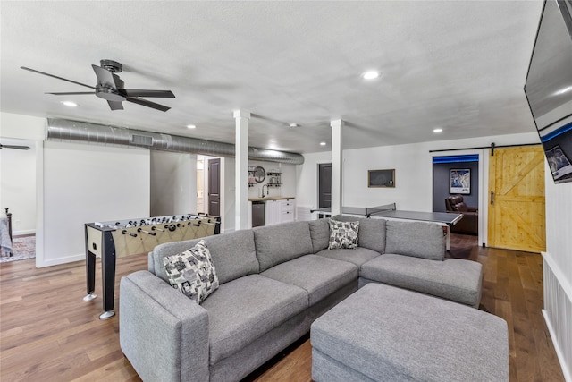 living room with a barn door, hardwood / wood-style flooring, ceiling fan, and a textured ceiling