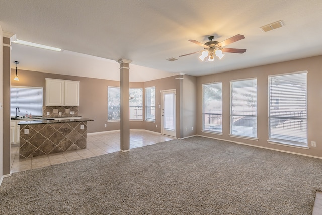 unfurnished living room with decorative columns, sink, light carpet, and ceiling fan