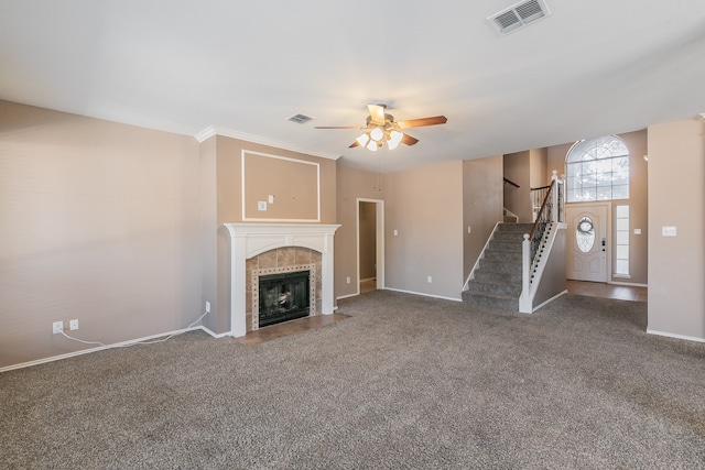 unfurnished living room featuring ornamental molding, a tiled fireplace, ceiling fan, and dark carpet